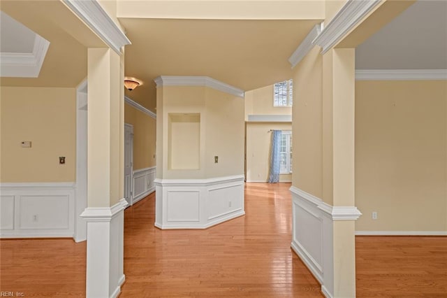 hall with crown molding, a decorative wall, light wood finished floors, and decorative columns