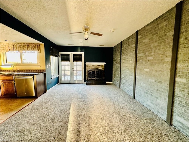 unfurnished living room with carpet floors, french doors, a fireplace with raised hearth, a textured ceiling, and brick wall