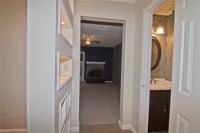 hall featuring a sink, baseboards, a textured ceiling, and carpet flooring