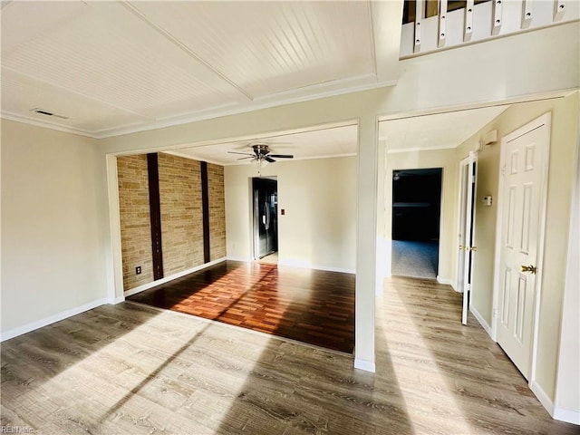 spare room with a ceiling fan, baseboards, brick wall, and wood finished floors