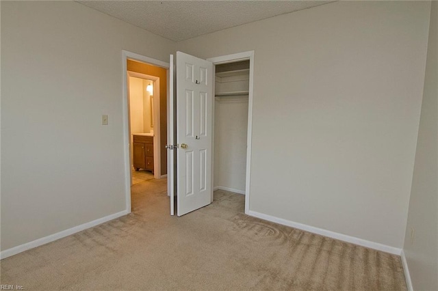 unfurnished bedroom featuring a closet, light carpet, a textured ceiling, and baseboards