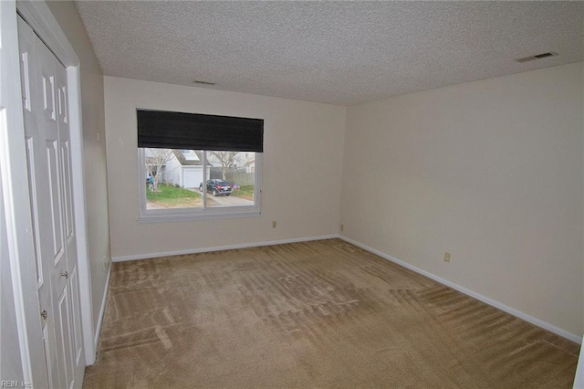 carpeted empty room featuring a textured ceiling, visible vents, and baseboards