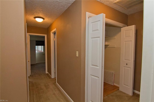 corridor featuring light carpet, visible vents, a textured ceiling, and baseboards