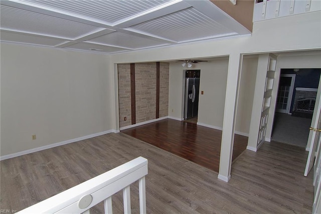 unfurnished room featuring brick wall, coffered ceiling, wood finished floors, a ceiling fan, and baseboards