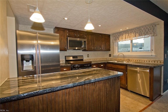 kitchen with hanging light fixtures, stainless steel appliances, dark brown cabinets, a sink, and light tile patterned flooring