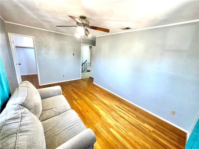 living room featuring ceiling fan, wood finished floors, visible vents, baseboards, and ornamental molding