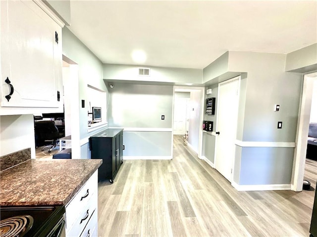 kitchen featuring light wood finished floors, dark countertops, visible vents, white cabinets, and black range with electric cooktop