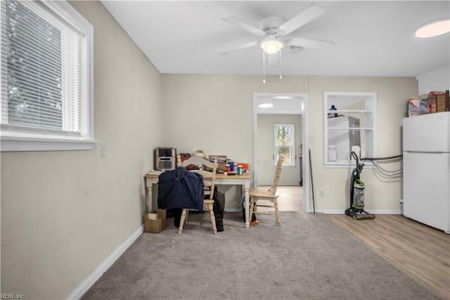 carpeted dining space featuring wood finished floors, a ceiling fan, and baseboards