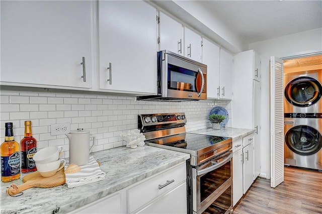 kitchen with stainless steel appliances, stacked washer / drying machine, backsplash, light wood-style flooring, and white cabinets