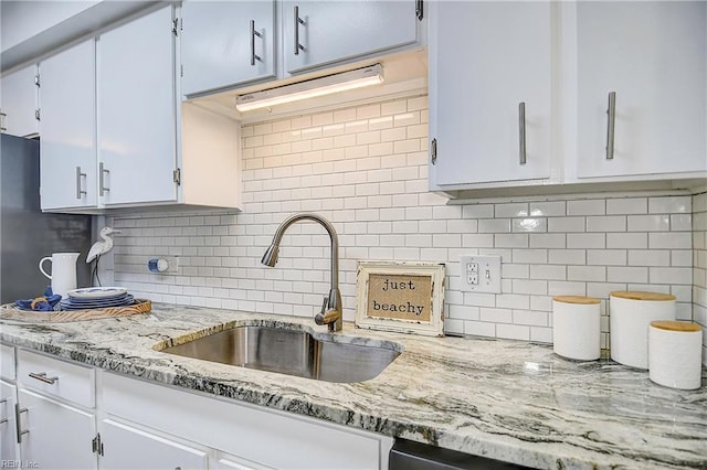 kitchen featuring white cabinets, a sink, decorative backsplash, and light stone countertops