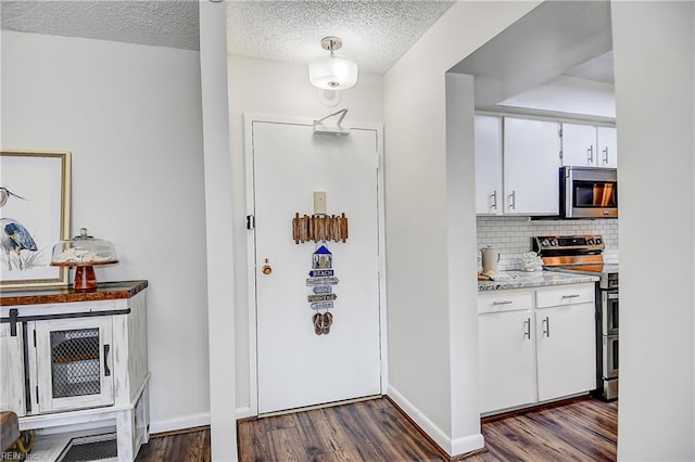 interior space featuring white cabinets, dark wood-style floors, stainless steel appliances, light countertops, and backsplash