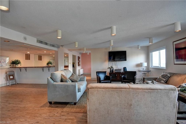 living room with a textured ceiling, visible vents, and wood finished floors