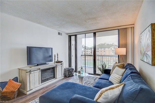 living area featuring a textured ceiling, a wall of windows, wood finished floors, and visible vents