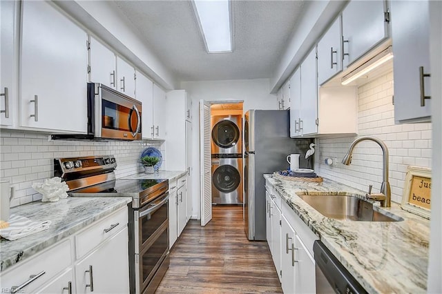 kitchen with dark wood finished floors, stacked washer and clothes dryer, appliances with stainless steel finishes, white cabinetry, and a sink