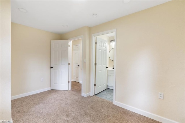 unfurnished bedroom with light carpet, ensuite bath, and baseboards