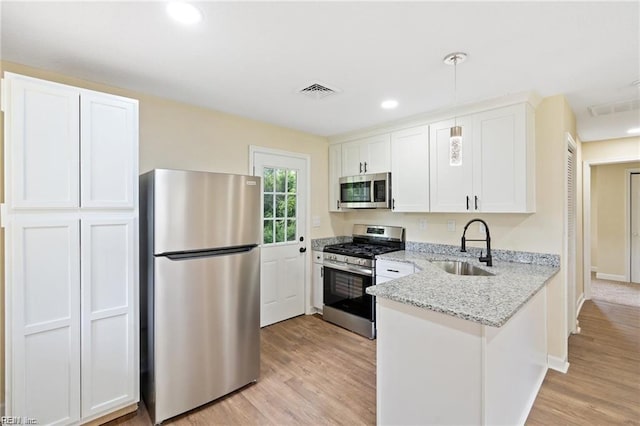 kitchen featuring stainless steel appliances, light wood-style floors, a sink, and a peninsula