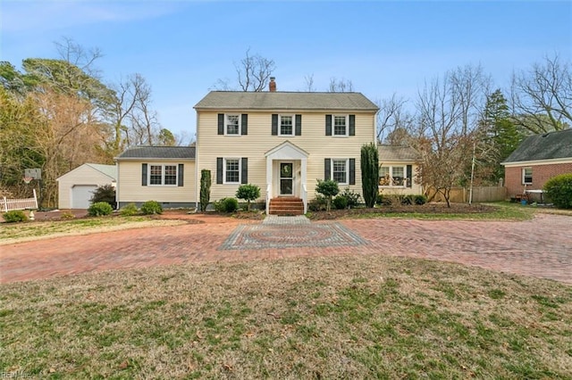 colonial house with an outbuilding, a detached garage, a chimney, a front yard, and fence