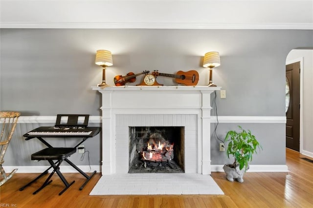 room details featuring a brick fireplace, crown molding, arched walkways, and wood finished floors