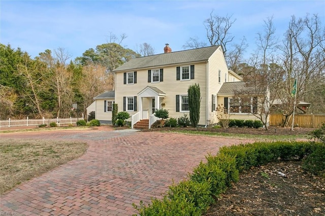 view of front of home with decorative driveway, a chimney, and fence