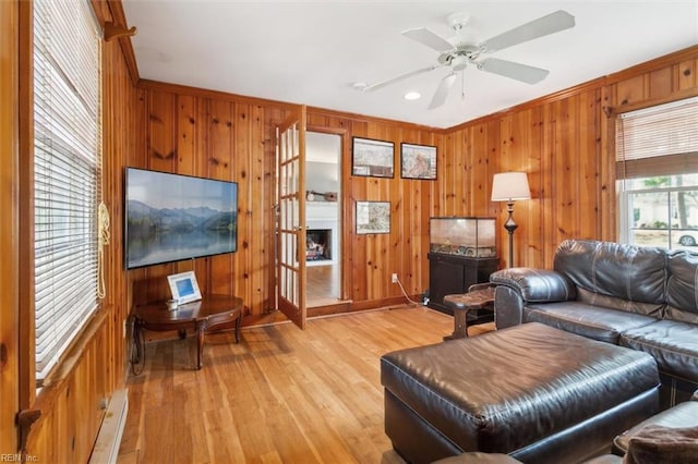 living area featuring ceiling fan, light wood-style flooring, wooden walls, ornamental molding, and baseboard heating