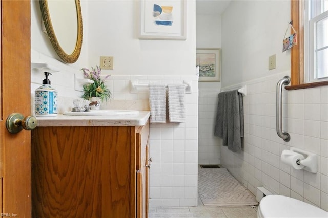 bathroom featuring toilet, a wainscoted wall, tile patterned flooring, vanity, and tile walls