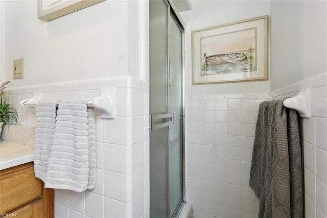 bathroom featuring wainscoting, a shower with shower door, tile walls, and vanity