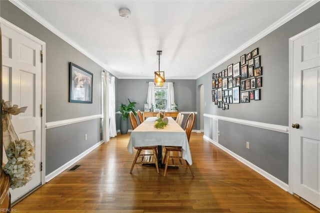 dining space with arched walkways, wood finished floors, visible vents, baseboards, and crown molding