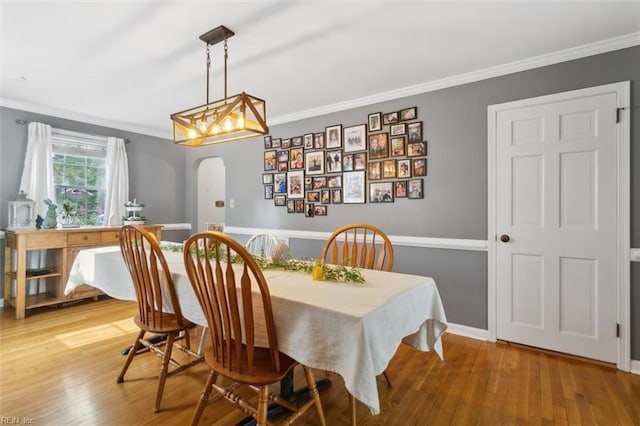 dining space featuring light wood-style floors, arched walkways, and crown molding