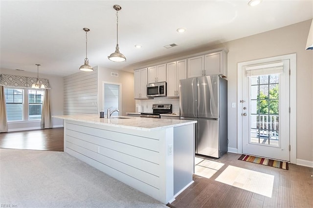 kitchen with stainless steel appliances, visible vents, backsplash, a kitchen island with sink, and a sink