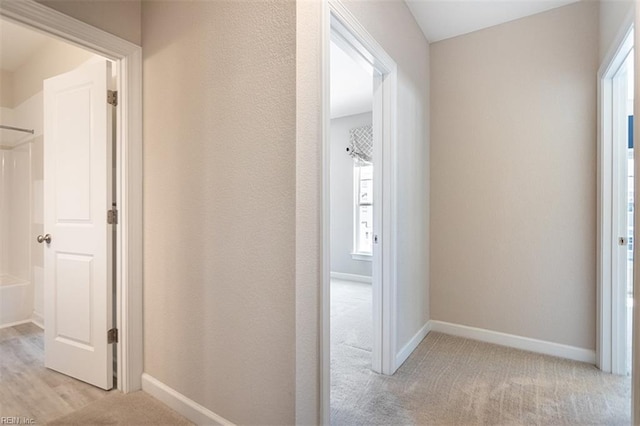 hall featuring light colored carpet and baseboards