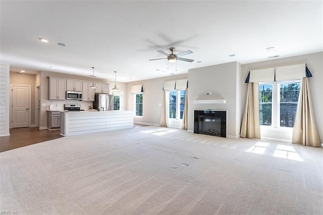 unfurnished living room with ceiling fan, recessed lighting, light colored carpet, baseboards, and a glass covered fireplace