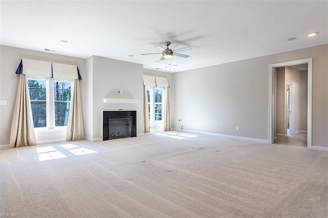 unfurnished living room with ceiling fan, a fireplace, baseboards, and light colored carpet