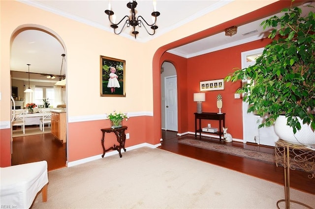 living area with baseboards, arched walkways, wood finished floors, crown molding, and a notable chandelier