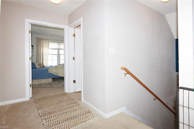 hallway with carpet floors, baseboards, and an upstairs landing