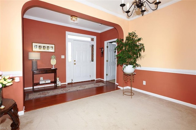 carpeted entryway featuring ornamental molding, arched walkways, a notable chandelier, and baseboards