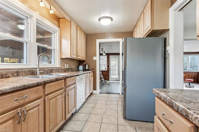 kitchen featuring light tile patterned floors, white dishwasher, a sink, freestanding refrigerator, and light brown cabinetry