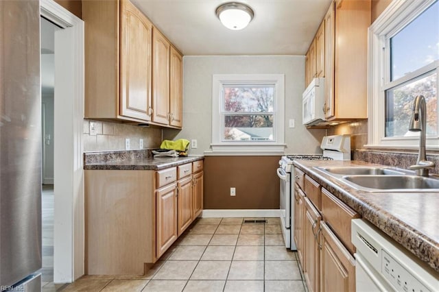 kitchen featuring a healthy amount of sunlight, white appliances, light tile patterned floors, and a sink