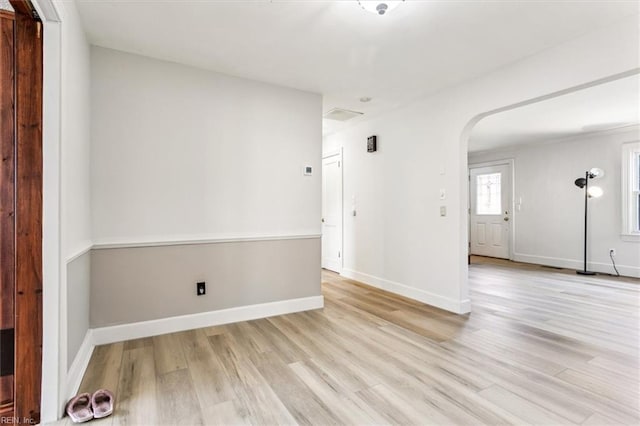 unfurnished room with arched walkways, light wood finished floors, and baseboards