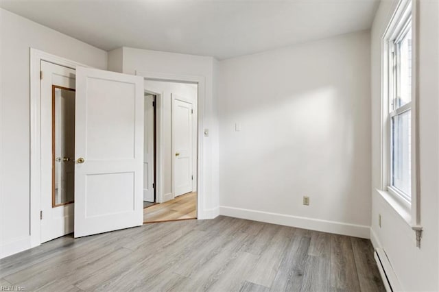 unfurnished bedroom with light wood finished floors, a baseboard radiator, and baseboards