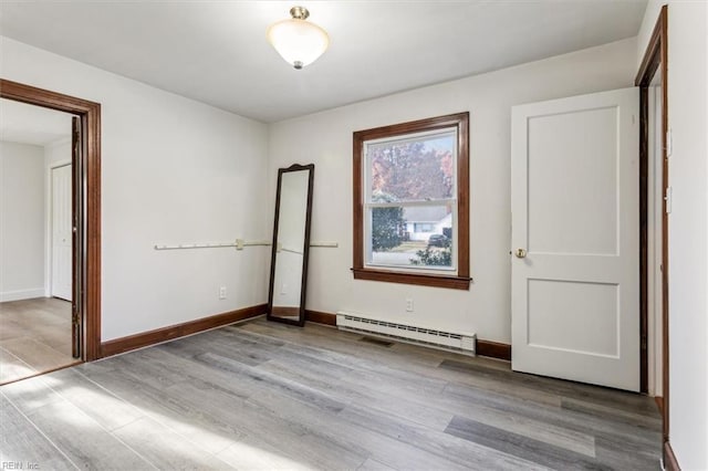 spare room featuring a baseboard radiator, wood finished floors, and baseboards