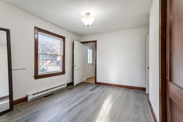 empty room with a baseboard heating unit, baseboards, and wood finished floors