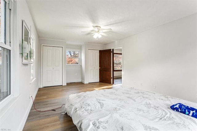 bedroom with baseboards, baseboard heating, two closets, and wood finished floors