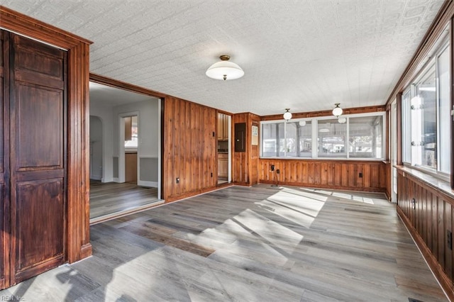 interior space with arched walkways, wood walls, baseboards, and wood finished floors