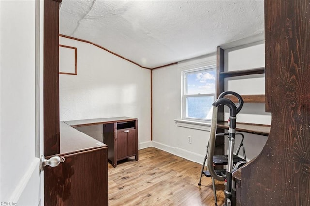 exercise area with light wood finished floors, baseboards, and a textured ceiling