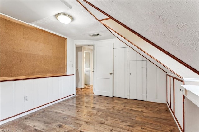 additional living space featuring a textured ceiling, visible vents, vaulted ceiling, and wood finished floors