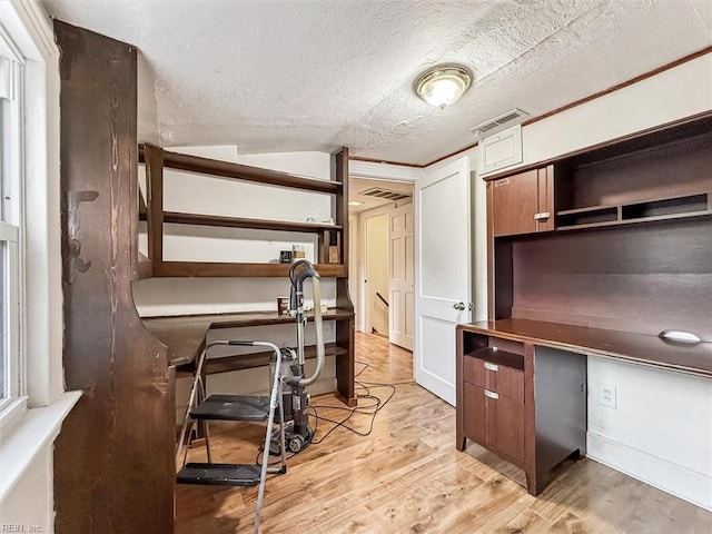 home office with light wood finished floors, built in desk, a textured ceiling, and visible vents