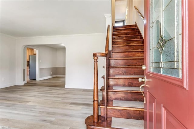 stairs with baseboards, crown molding, arched walkways, and wood finished floors