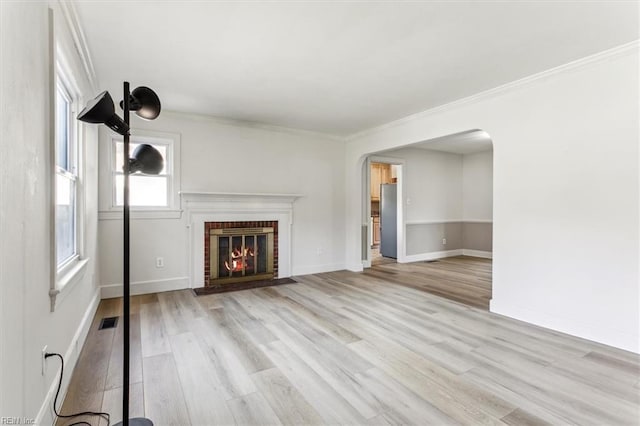 unfurnished living room with arched walkways, light wood-style flooring, visible vents, a brick fireplace, and crown molding