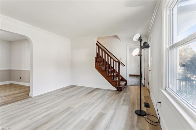 empty room with arched walkways, light wood-style flooring, visible vents, stairs, and crown molding