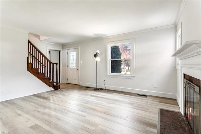 unfurnished living room with a brick fireplace, light wood-style flooring, stairway, and ornamental molding